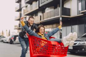 man riding girl on shopping trolley on parking